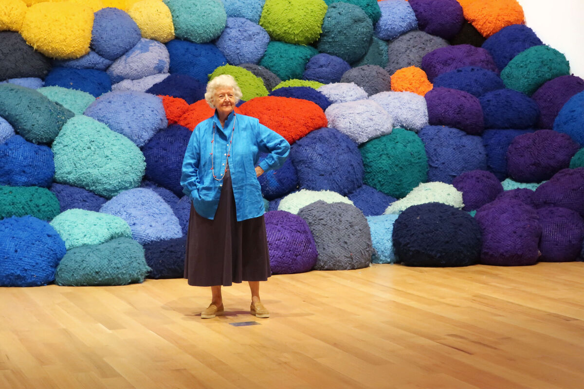 Portrait of Sheila Hicks in front of Escalade Beyond Chromatic Lands (2016-2017), “Campo Abierto (Open Field)” at The Bass Museum of Art, 2019. Photo by Mudita.