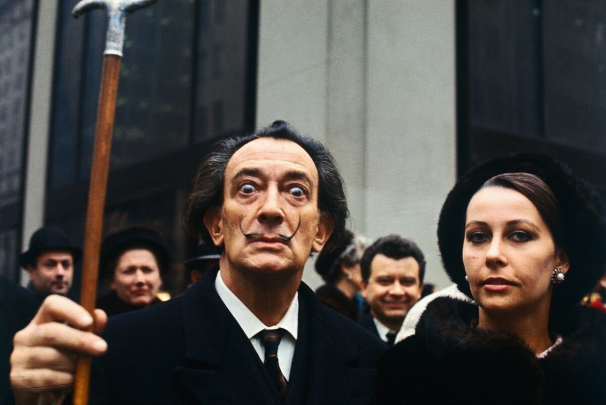 Artist Salvador Dali, lifting his cane, in a crowd. Image via Getty Images.