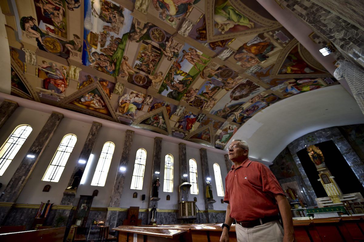 Miguel Francisco Macías muestra las copias de pinturas originales de Miguel Ángel en la Capilla Sixtina que reprodujo en la iglesia de Nuestra Señora del Perpetuo Socorro. Foto por Yuri Cortez / AFP / Getty Images.