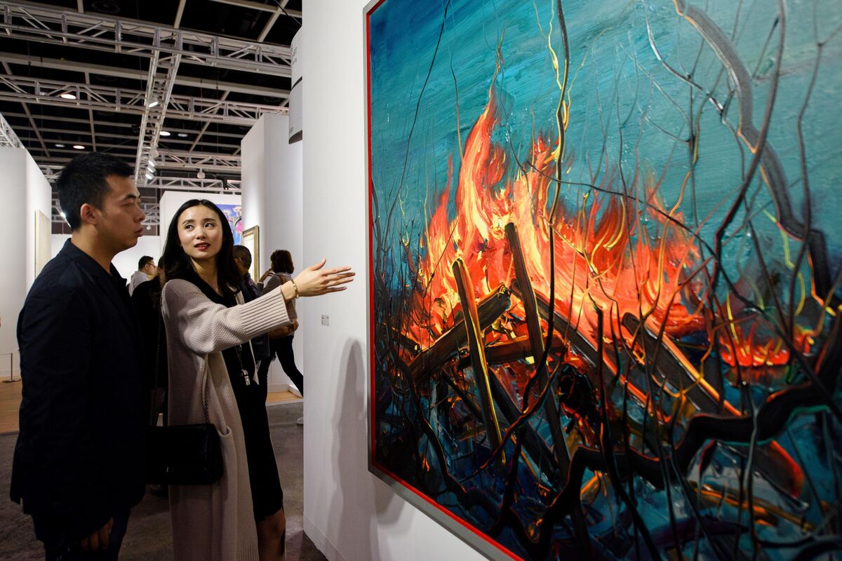 Investment banker Huang Xiaoshuai and his wife Wei Mengyuan chat in front of their newly acquired painting Fire by Chinese artist Zeng Fangzhi at Art Basel in Hong Kong. Photo by Anthony Wallace/AFP/Getty Images.