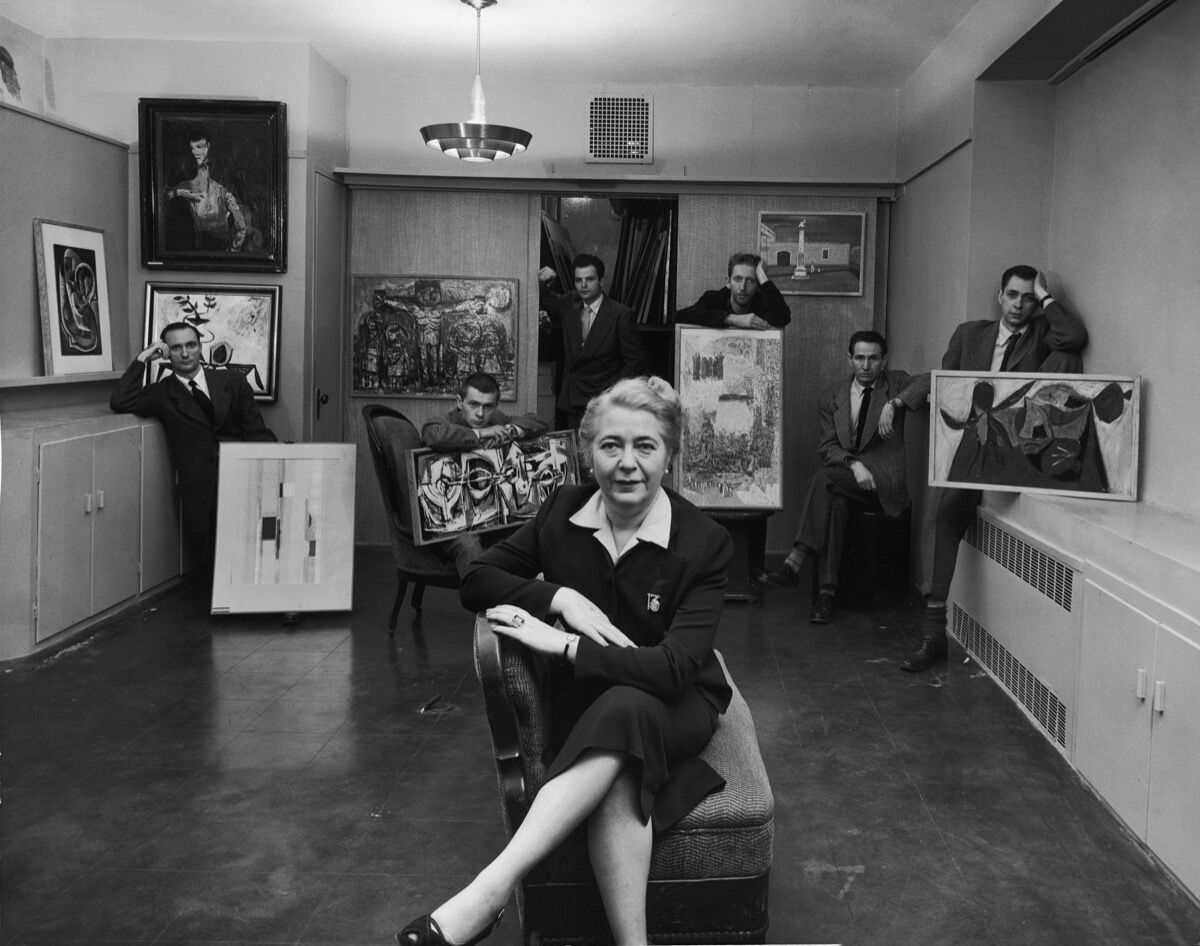 Edith Halpert at the Downtown Gallery, wearing the 13 watch brooch and ring designed for her by Charles Sheeler, in a photograph for Life magazine in 1952. She is joined by some of the new American artists she was promoting that year: Charles Oscar, Robert Knipschild, Jonah Kinigstein, Wallace Reiss, Carroll Cloar, and Herbert Katzman. Photo © Estate of Louis Faurer. Courtesy of the Jewish Museum.