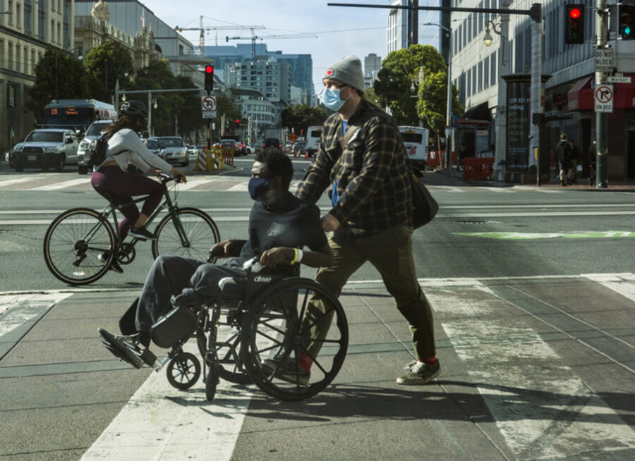 COVID-19 masked man pushing masked amputee in wheelchair along Market Street, San Francisco