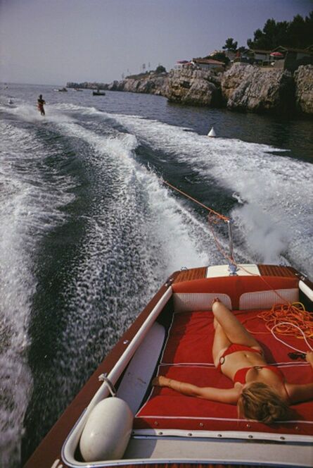 Slim Aarons, ‘Leisure in Antibes, 1969: A woman sunbathes on a motorboat as it tows a waterskier in the bay off the Eden-Roc’, 1969