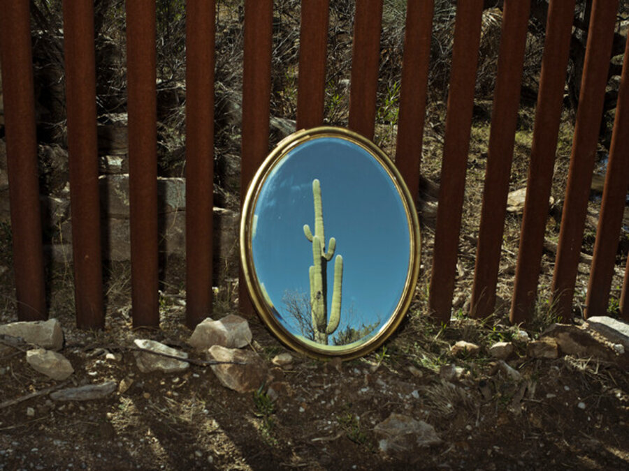 A cactus is reflected in a mirror placed leaning on the border fence near Nogales