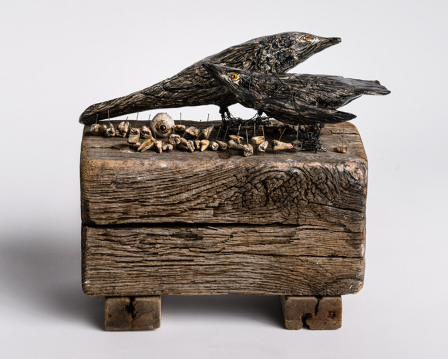 Sculpture of black birds on wood base with body parts: 'When the grackles took over'
