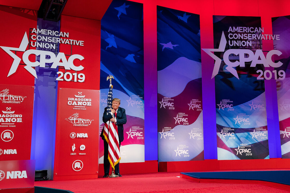 U.S. President Donald Trump hugged a U.S. flag at the Conservative Political Action Conference on March 2, 2019. Photo by Official White House Photo by Tia Dufour, via Flickr.