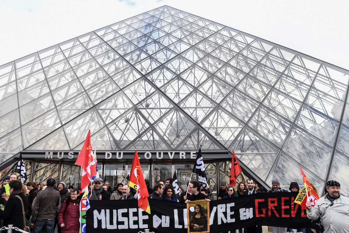 Protesters outside the iconic pyramid designed by I.M. Pei  at the Louvre museum hold a banner that reads, in French: “Louvre Museum on Strike.” Photo by Alain Jocard/AFP via Getty Images.