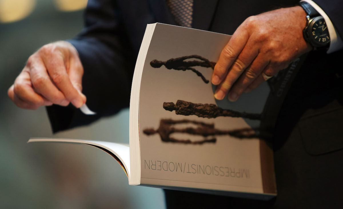 A guest holds a catalog before entering a Christie’s sale in New York. Photo by Mario Tama/Getty Images.